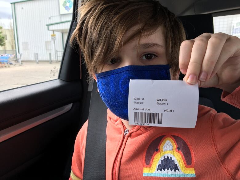 A brown-haired boy wearing a medical mask holds up a receipt for $40.35 from an Edmonton bottle depot. 