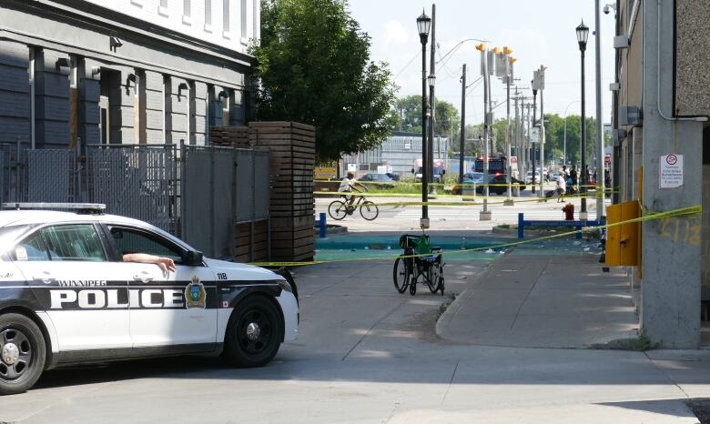 A wheelchair sits behind police tape in an alley.