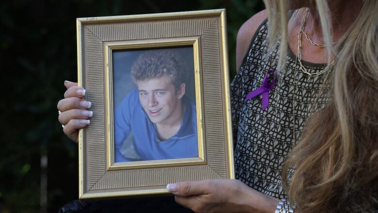 A woman holds a picture frame with a photo of her young son in it. He has light curly hair and a friendly smile.