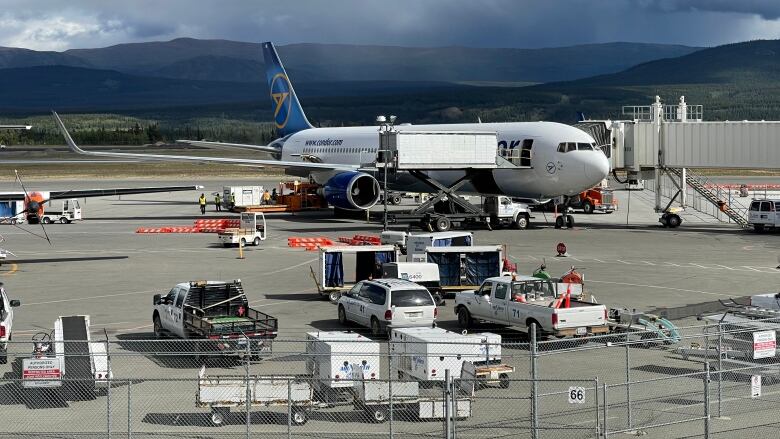 A plane is parked at the airport in Whitehorse, with mountains and rain patches in the background.