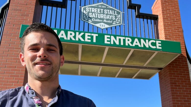 Man stands in front of the gate to market square in Saskatoon, which reads 