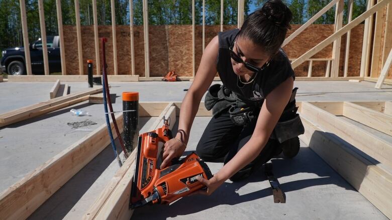 A carpenter kneels and staples a two-by-four.