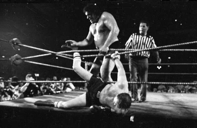 Wrestler Andr the Giant tosses heavyweight contender Chuck Wepner over the rope of the ring with the referee in the background.