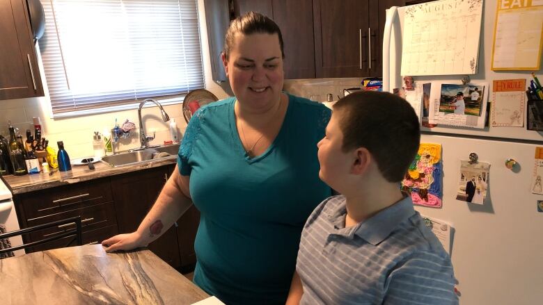 A woman smiles at a boy who is seated at a kitchen island 