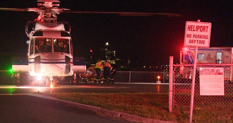 A helicopter sits on a tarmac as an injured worker is wheeled to a waiting ambulance.