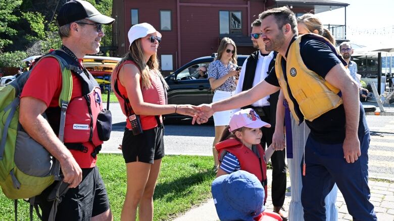 A man in a life jacket shakes hands with a woman, also in a life jacket, while alongside his family. 