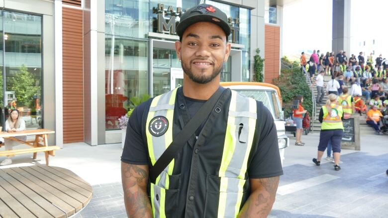 A portrait of a man in a brightly coloured vest standing on a city stidewalk.