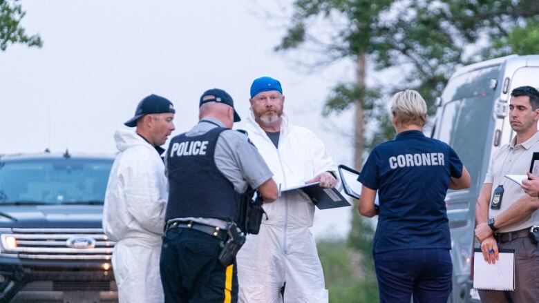 Police officers and coroners stand in a circle in an open area.