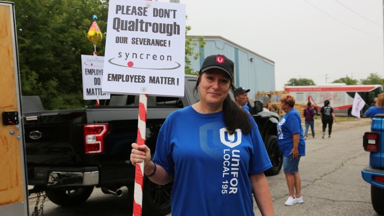 A woman wearing a hat and a blue t-shirt holding a sign requesting money from the federal government