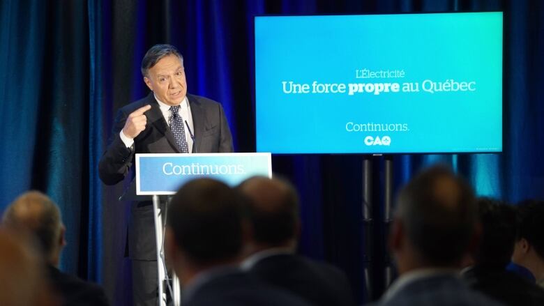 A man stands at a podium in front of a screen touting electricity as clean power.