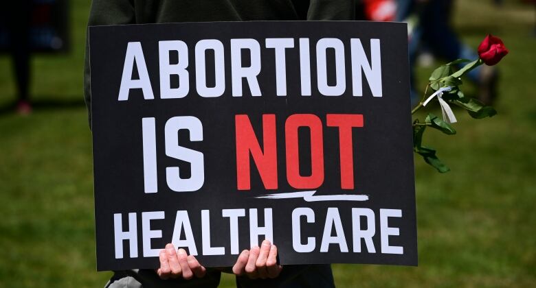 A protester holds a sign that reads 'Abortion is not health care.'