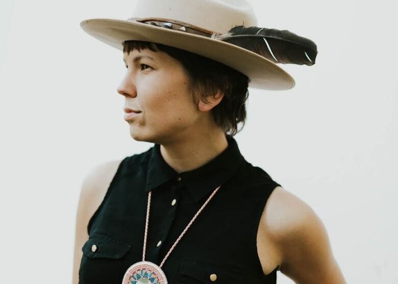 A woman wearing a wide-brimmed hat with a feather in the hatband poses.