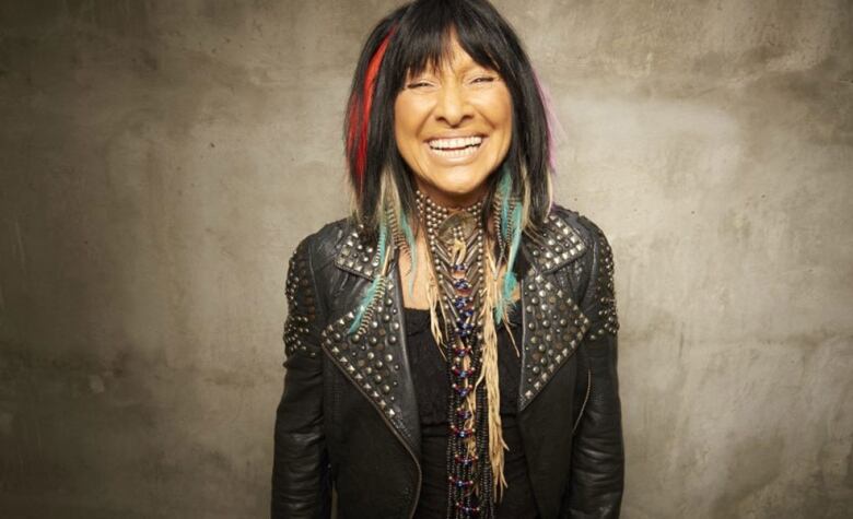 A woman with a bright red streak in her dark hair, wearing a studded leather jacket, smiles widely.