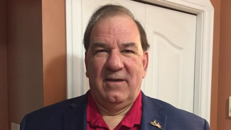 A portrait of a man with dark hair, wearing a red collared shirt and blue blazer.