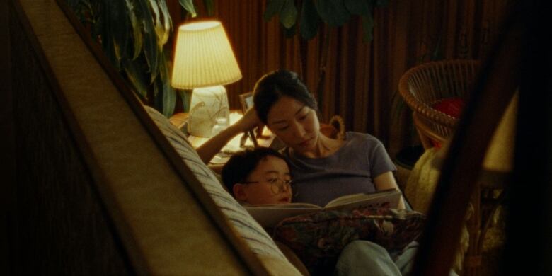 A Korean mother reads to her young son on a sofa at night.