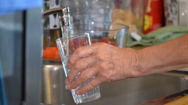 A hand fills up a glass from a sink.