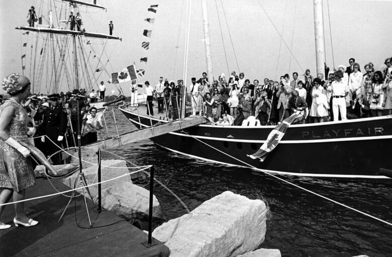 A black-and-white photo of a crowd on a dock around a sailing vessel.