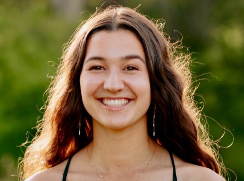 Emily Selwood was 18 years old and just starting her studies in social sciences at UBC when she was killed by an alleged drunk driver on Sept. 26, 2021. An undated family photo shows a smiling young woman from the shoulders up in bright sunlight. She has long brown wavy hair and dark eyes, and is wearing a spaghetti strap top, dangly earrings and a thing gold necklace.