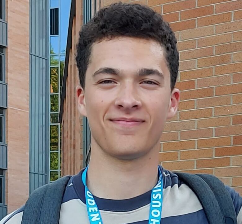 Evan Smith, 18, was a first year engineering student at UBC when he was killed by a suspected drunk driver on Sept. 26, 2021. A family photo shows a young man with a slight smile standing in front of a brick building. He has curly brown hair and is wearing a striped t-shirt with a backpack on top.