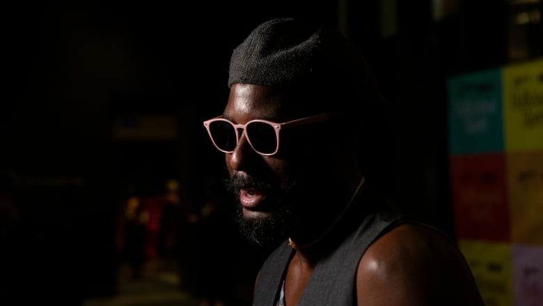 Man in glasses stands on red carpet talking.