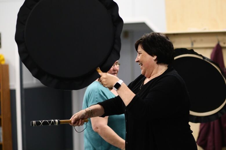 A woman in black holds a large black Inuit drum