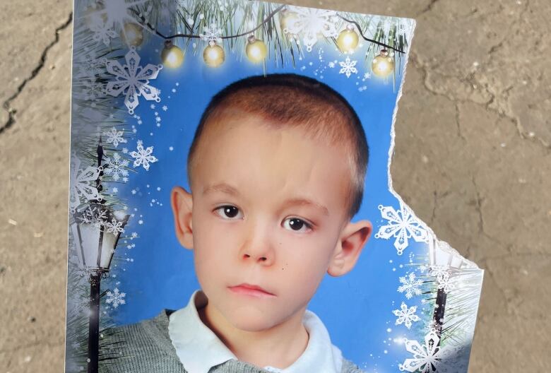 A serious looking young boy poses for a photo with a winter border featuring cartoon characters in the style of Pixar's Cars. 