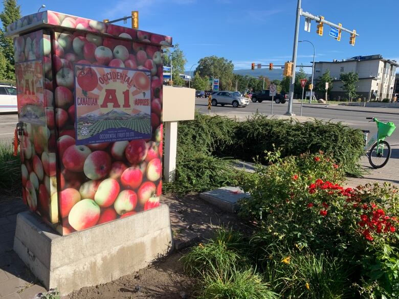 A utility box with red apple packaging on a street corner.