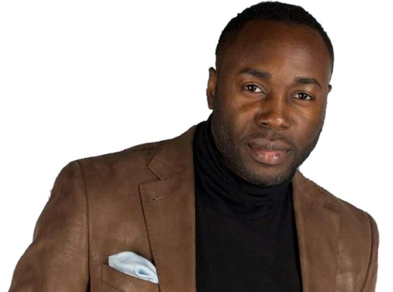 A headshot of a man in a tan blazer and black turtleneck.