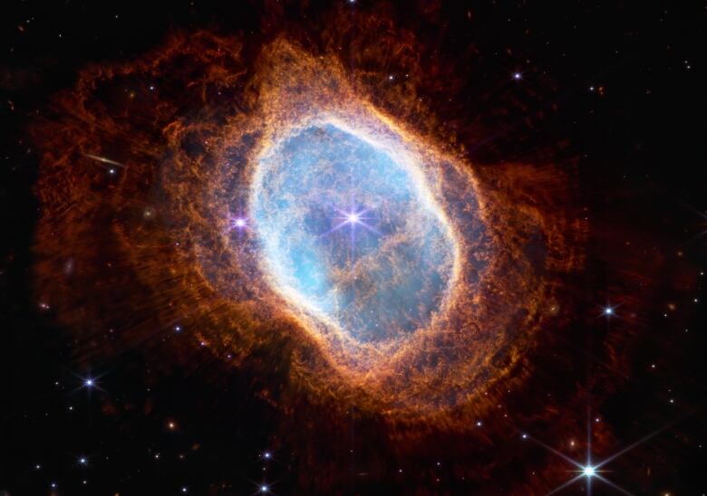 An orange nebula with a blue centre is seen against the blackness of space with a few stars in the background.