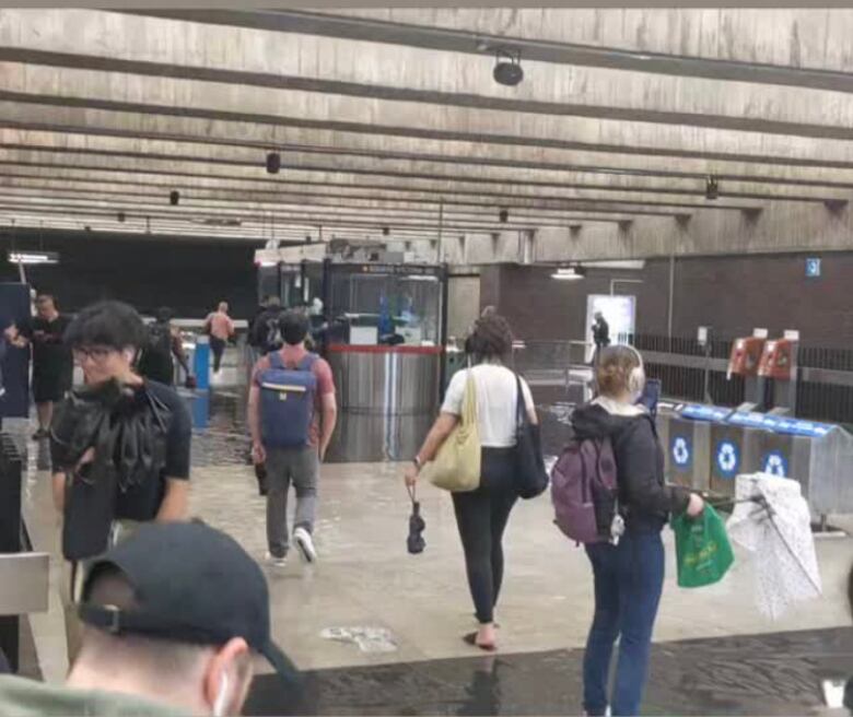 Water on the tiled floor, people walking near turnstiles.