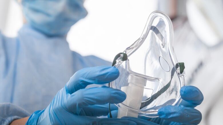 A respiratory therapist with blue-gloved hands holds out an oxygen mask.