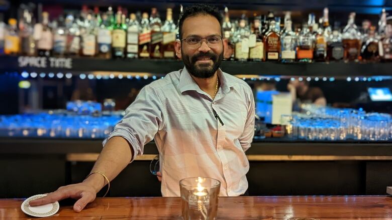 A man smiles from behind a bar.