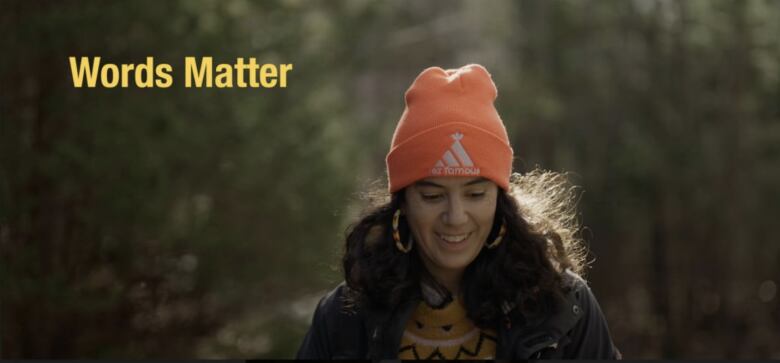 Woman smiling while walking in the woods, wearing an orange toque over her long black hair.