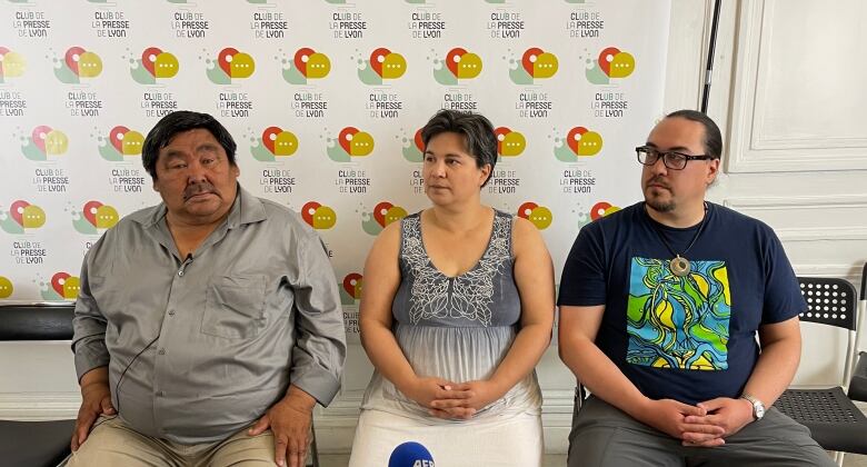 Three people sit on chairs with their hands in their laps.