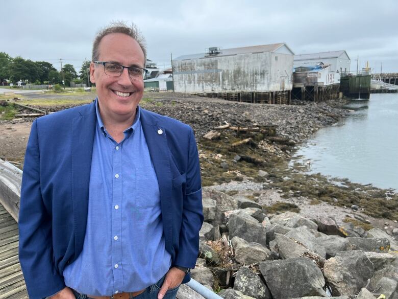 A man wearing glasses poses for a photo in front of the shoreline.