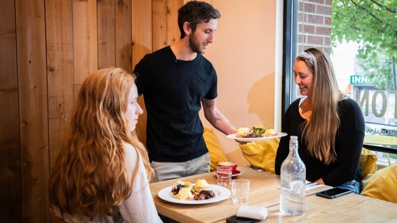 A server gives food to two white women in a restaurant.