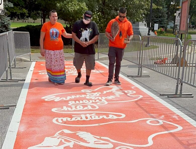 Three people walking across an orange crosswalk with the words 