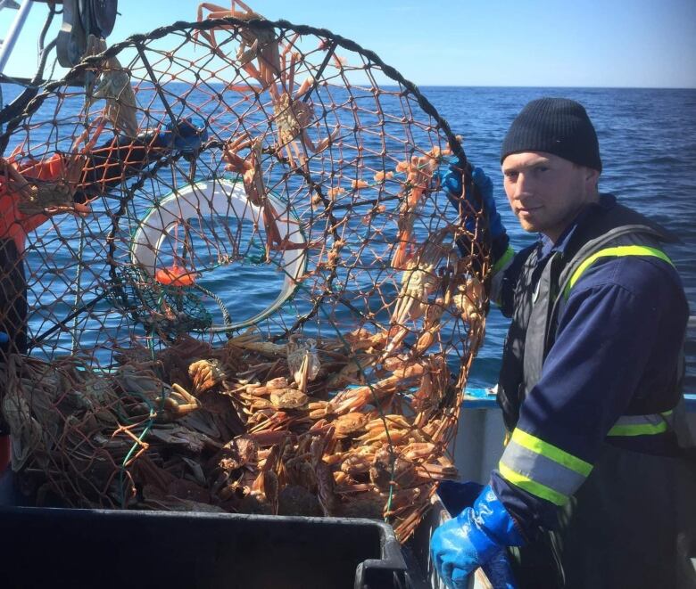 A man in blue coveralls holds a bucket of crabs on a boat 