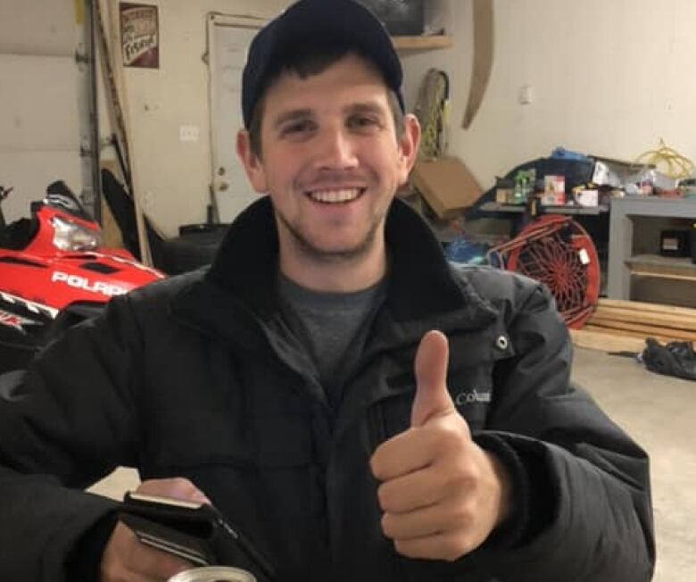 A man in a black jacket holds a thumbs up to the camera. 