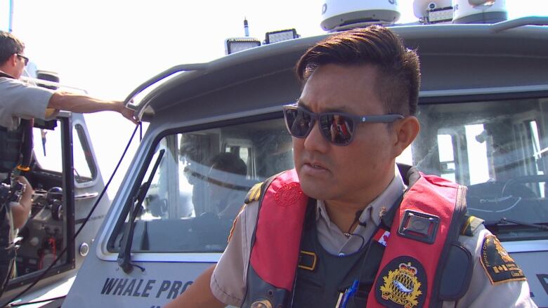 An officer with a life vest on gestures in a boat.