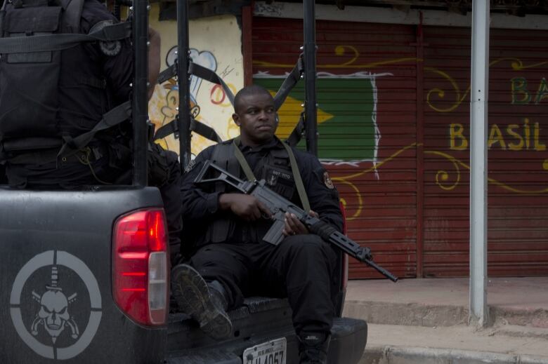 A uniformed man holding a large gun sits in the back of a truck. 