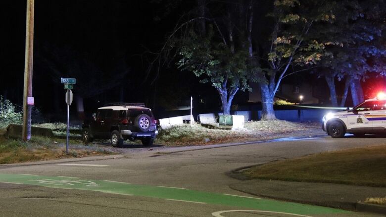 A black jeep is seen off to the side of a road, with a cop car flashing its lights in the background.