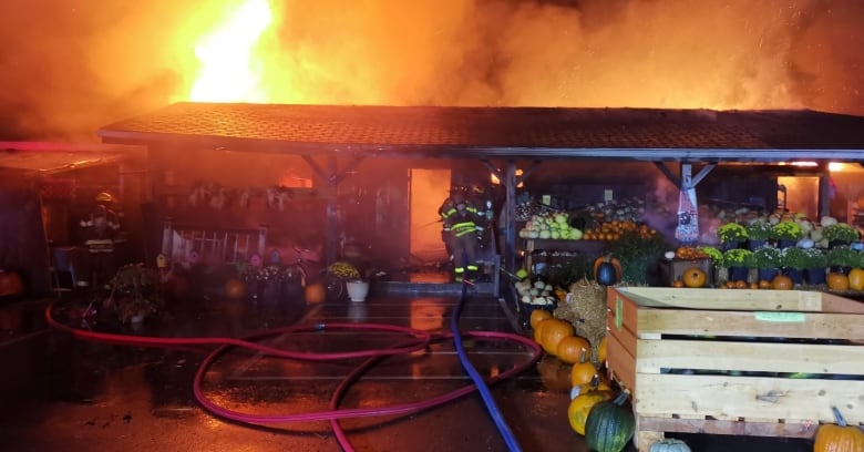 A large flame in the background rises from a one-storey building with stands of pumkins and gourds in the fireground.