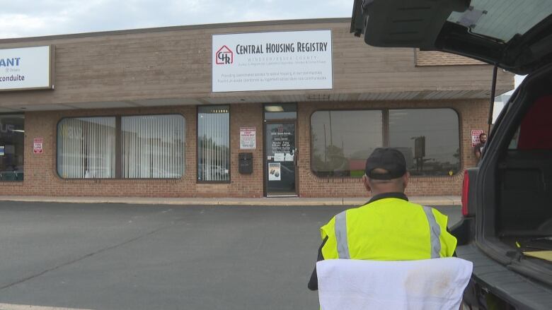 A man sits facing a building that has a sign that says Central Housing Registry. 