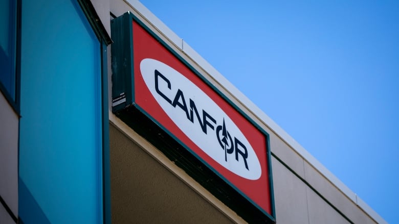 A red sign with a white oval that says Canfor.