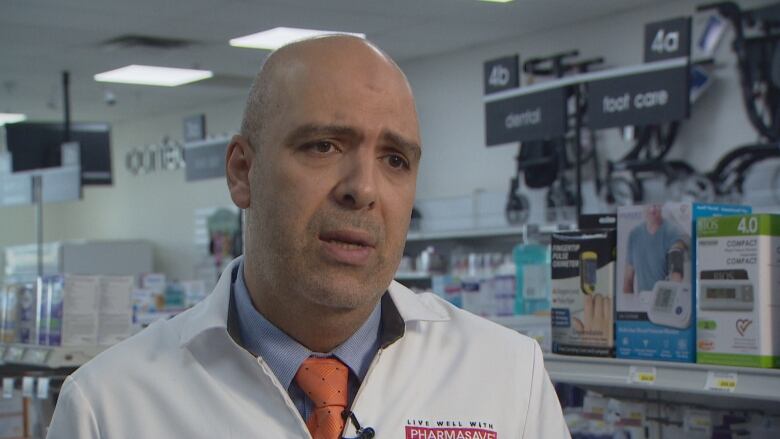 A man in a white coat stands in a pharmacy. 