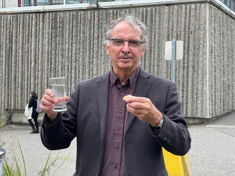 A man holding a glass of water and a muffin. 