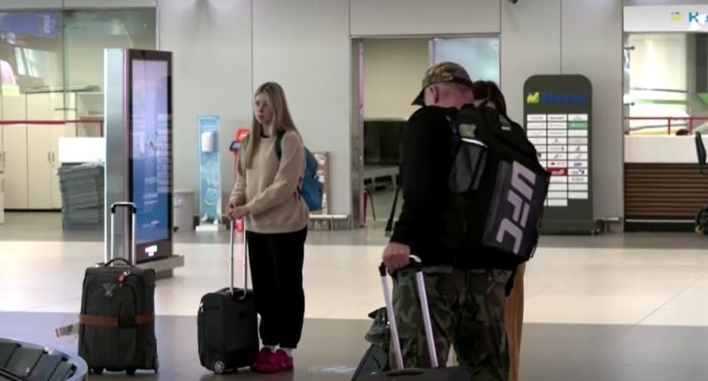 Three people stand with suitcases in an airport.