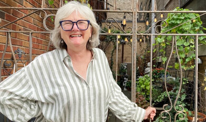 Portrait of woman in front of red brick alleyway that has lots of plants and patio lights.