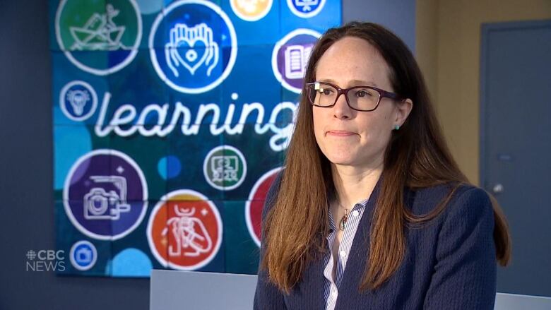 A woman in glasses in front of a sign that says 'learning'. 